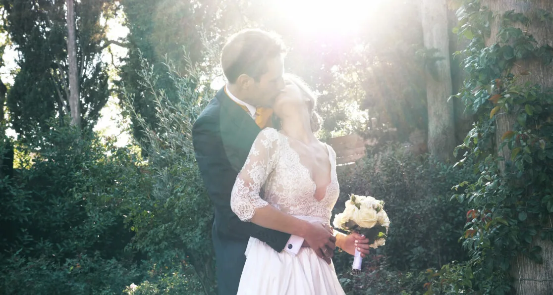 Couple avec le marié derrière la mariée et qui s'embrassent.