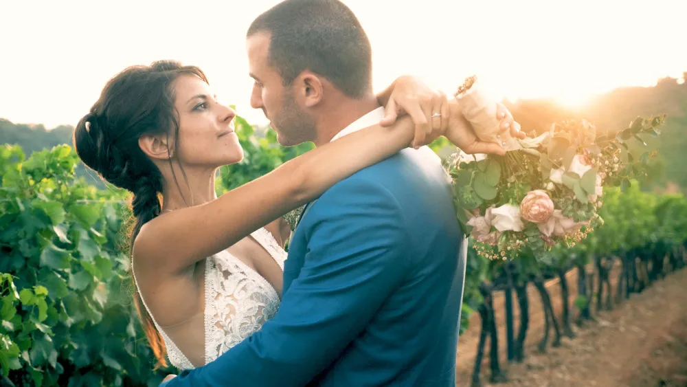 Couple de mariés s'enlaçant dans les vignes au soleil couchant.