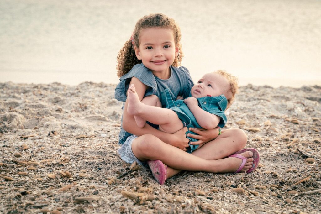 Fillette qui tient un bébé dans ses bras assise sur la plage
