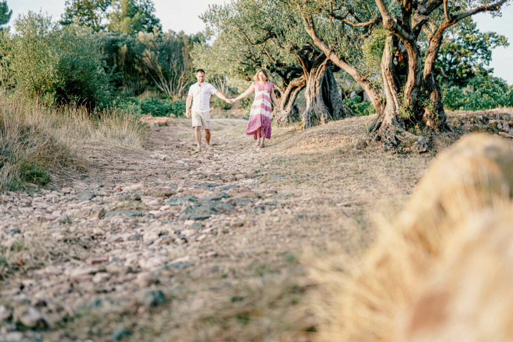 Couple avec femme enceinte avec robe colorée marchant main dans la main avec une haie d'olivier sur le côté.
