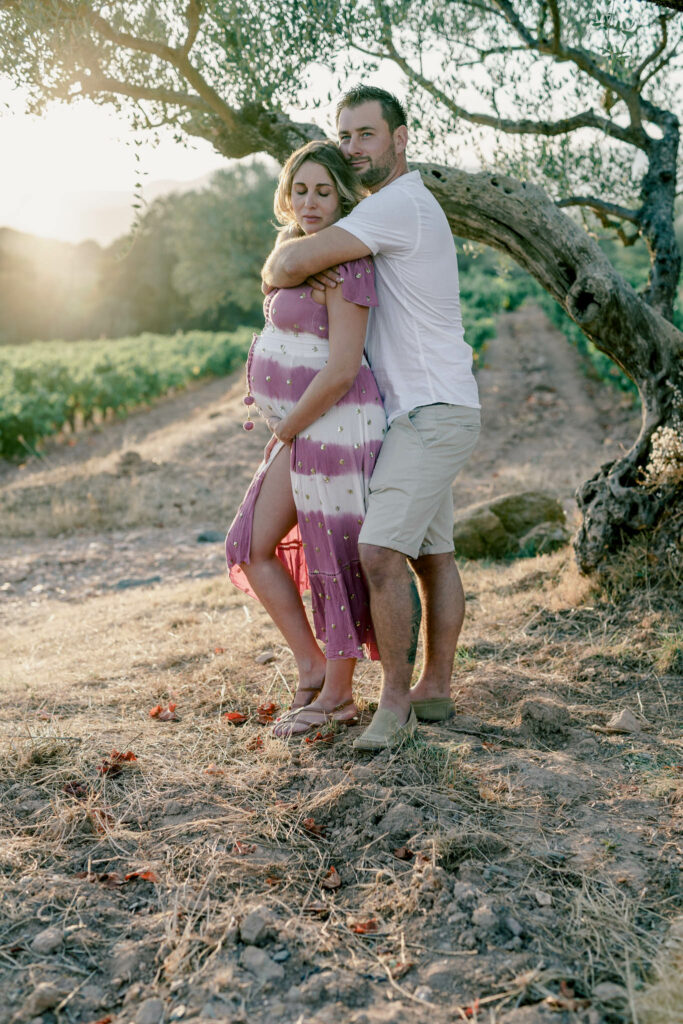 Couple avec femme enceinte avec robe colorée s'enlaçant à côté d'un olivier.